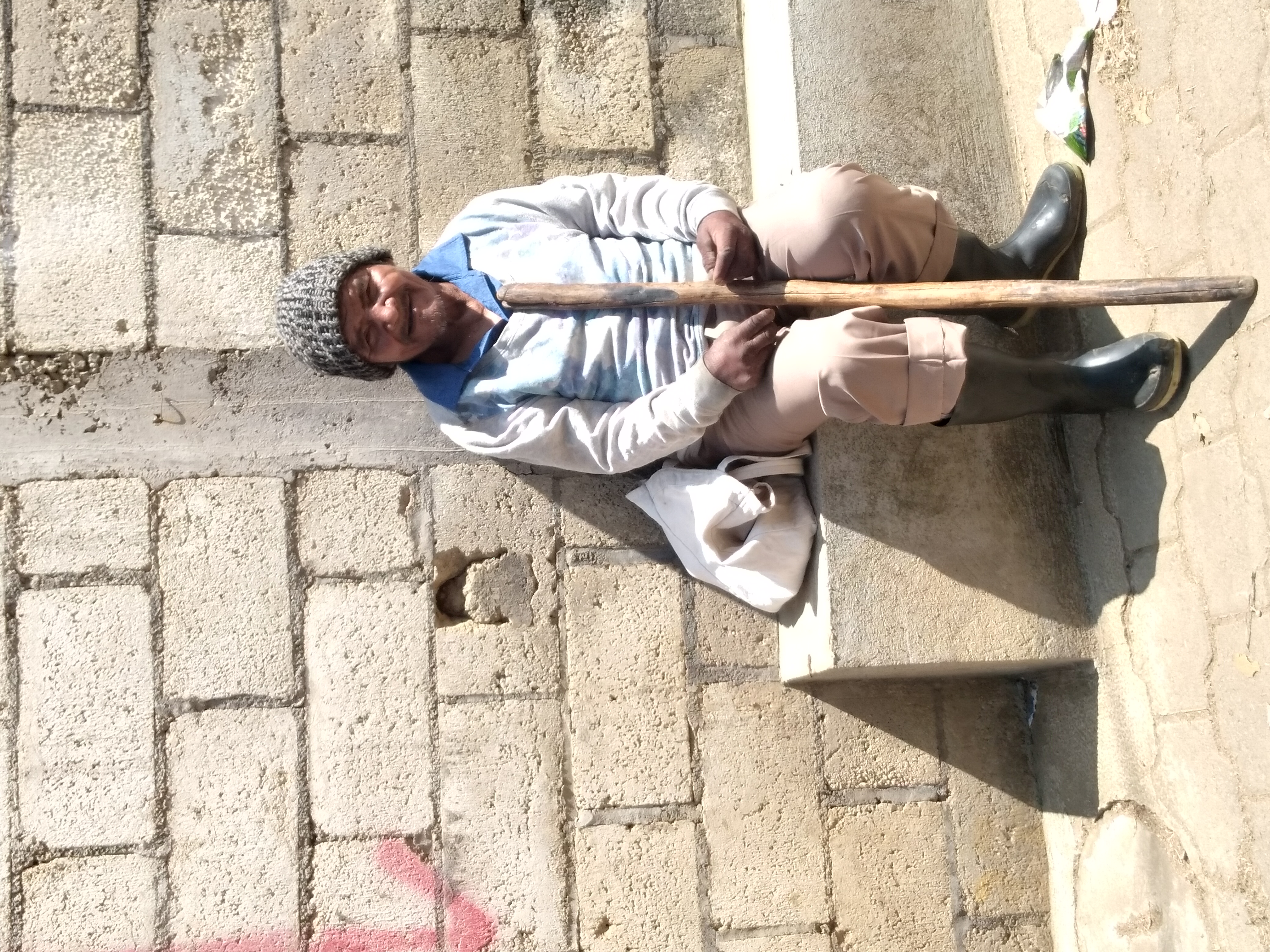 A man with a stick sitting by a wall.